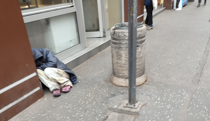 Фотографија бескућника који покушава да се загреје прибијен уз излог пекаре, Београд, октобар 2023